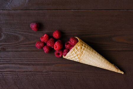 Waffle cone with fresh organic raspberries on a brown wooden backgroundの写真素材