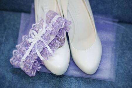 White wedding shoes for the bride and a purple garter on a blue background. Accessories for the brideの写真素材