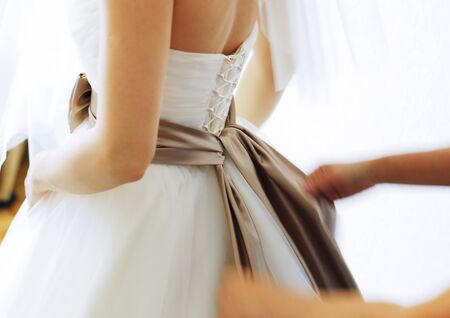 Morning of the bride. A friend ties a bow on the bride's dress. Selective focus.の写真素材
