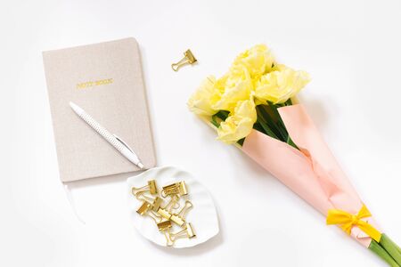 Office Desk with a notebook, yellow flowers, clips, white pen with dots for paper on a white...