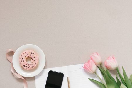 flat lay blogger or freelancer with delicate pink tulips, office supplies, Donat and phone on a...