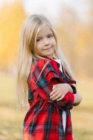 Portrait of a little girl in a red checked shirt with blonde hair in an autumn Parkの写真素材
