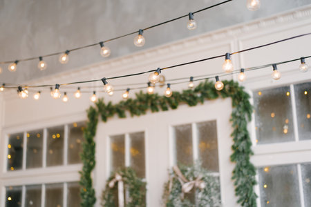 A retro garland of incandescent lamps is lit against the background of the entrance doors to the house, decorated with Christmas wreathsの写真素材