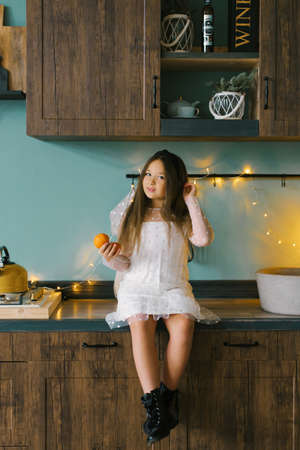 Portrait of a cheerful little girl with tangerines in her hands in the Christmas kitchen, cozy home