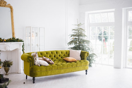 The green velor sofa with pillows in the bright attic room has an artificial fireplace.A spacious living room with white walls and a decorated Christmas treeのeditorial素材