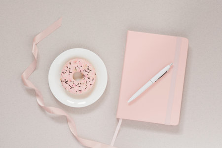 A delicate and beautiful banner: a pink donut on a white plate and a pink diary with a white pen on a dusty coffee background. Trending minimalistic design for blogger or freelancerの写真素材
