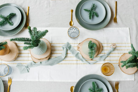 Christmas table setting. Spruce branches on plates and in vases with gold Cutlery on a light linen tablecloth.の写真素材