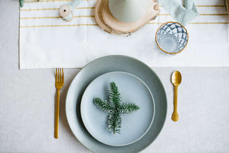 Spruce branch on a plate as part of the table setting with a gold fork and spoon, linen tablecloth,...