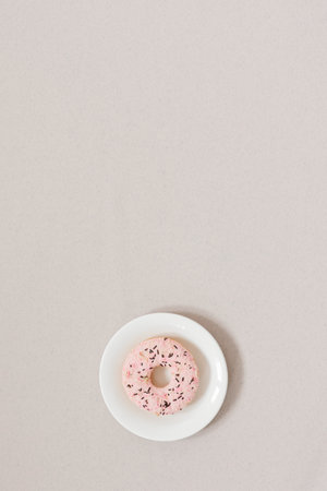 Minimalistic sweetness banner. pink donut on a white plate on a beige background with copy space. Morning or dinner dessert. The background for the blogの写真素材