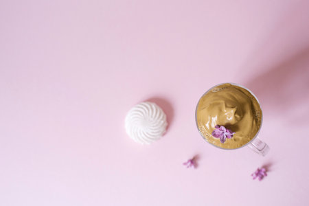Beautiful dalgon coffee drink. Coffee mug with foam and lilac flower on a lilac pink background. Top viewの写真素材