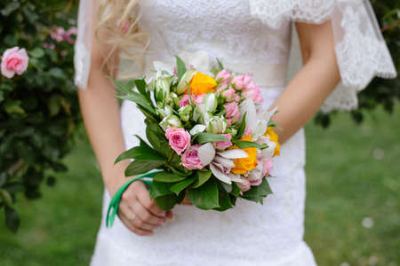 Delicate beautiful wedding bouquet of pink and yellow roses and orchids with greenery in the hands...