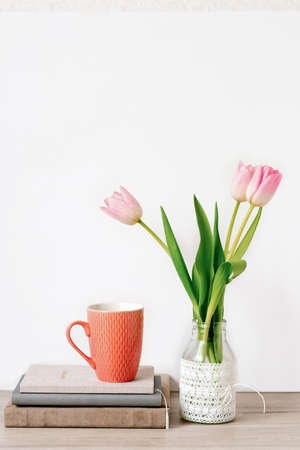 A bouquet of three pink tulips stands in a glass vase with lace. Next to it are notebooks or notepads with a ceramic mug of tea. Greeting card for Mother's Day, Valentine's Day, Teacher's Day. The concept of springの写真素材