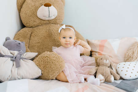A cute one year old baby sits surrounded by soft animals toys and pillowsの写真素材