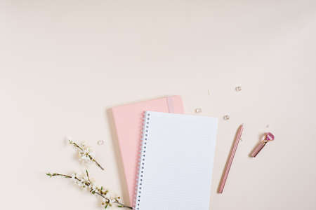 A blank notebook sheet with a sprig of white apple blossoms, a pink notebook and a pink pen on a...
