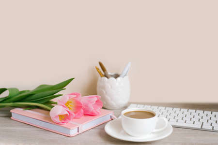 Pink tulips with a festive spring mood and coffee on a wooden table Women's work, home office and career concept. Side view. Copy spaceの写真素材