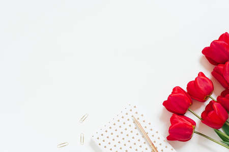 Workplace with notepad, red tulips, pen, paper clips on a white background for Valentine's Day or Mother's Day. Flat bed, top viewの写真素材