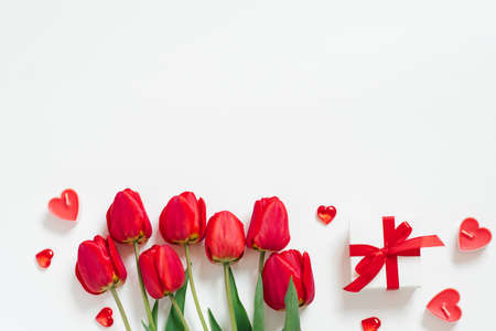Valentine Day Romantic Background. Red tulips, a gift with a bow, and candle hearts on a white...