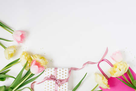 Beautiful Spring pink and yellow tulips flowers with white ribbon with bright bag on white. Flat...