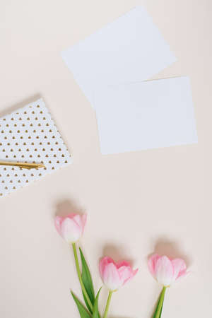 Work space concept with clipboard, notebook, pen, pink tulip flowers and accessories on beige...
