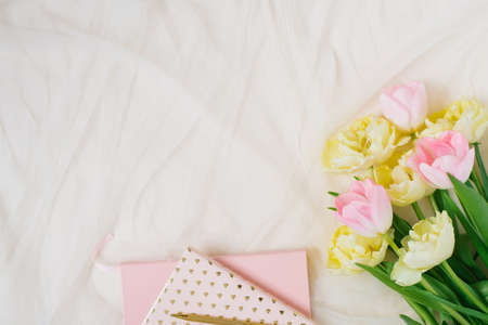 Pink notebooks and pink yellow tulips on beige background. Woman's workplace in pink. Flat lay for Valentine or Marther Day. Top view. Copy spaceの写真素材