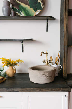 Retro stone sink and mixer golden in the kitchen in the Scandinavian style, a bouquet of mimosa in a clay vaseの写真素材