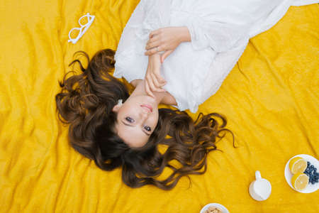 Top view of a beautiful romantic woman in a dress, lying on the green grass on a yellow blanket....