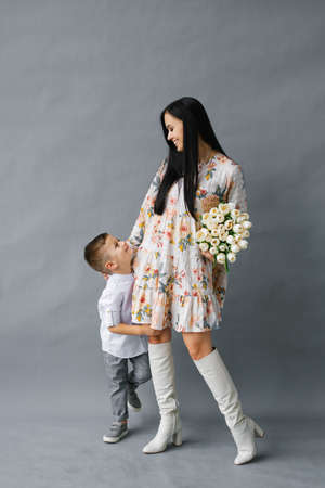 Portrait of a young mother with a small child standing on a gray background, family love and sincerityの写真素材