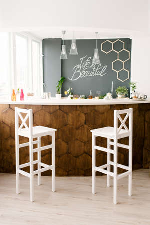 A stylish modern bar counter decorated with wooden tiles and two white bar stools in the living room...