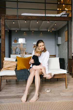 Young mom hugs her little daughter while sitting on the couchの写真素材