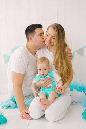 A beautiful young happy family with a one-year-old child, the Father kisses the mother on the cheek, the child is strong in the mother's arms. Happy parents and sonの写真素材