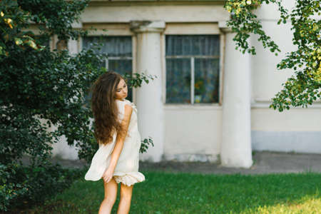 A young woman with long hair runs through the grass in the city park in summer, her hair fluttering in the wind.の写真素材