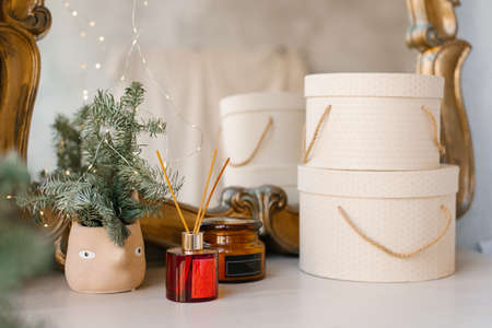 Home Christmas decor: diffuser, hat gift boxes, fir or spruce branches in a ceramic vase on the...