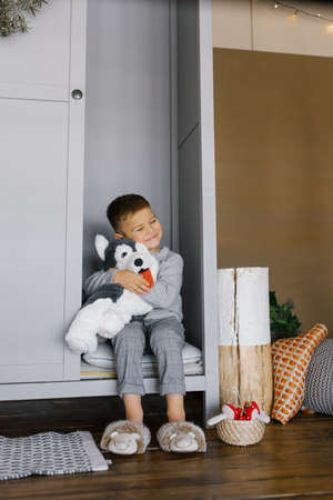 A little boy is sitting in the closet and hugging his favorite soft toy, he is happy and smilingの写真素材