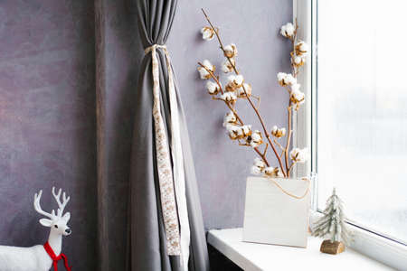 Cotton branches in a vase at the window. Christmas decor in the house. Cozy New Year and winterの写真素材