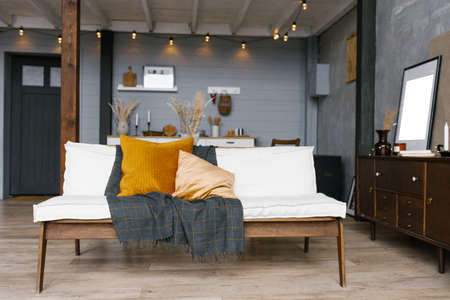 Stylish and Scandinavian interior of the living room of a modern apartment with a white sofa, pillows, a blanket, a kitchen in the background. Modern home decor.の写真素材