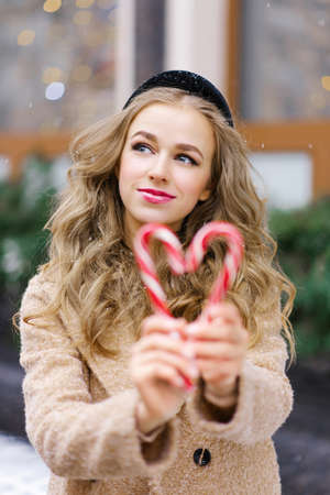 A sweet dreamy girl, a young woman holding a lollipop in the form of a heart on a winter day. The concept of Christmas or Valentine's Dayの写真素材