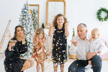 A European young family, dad, mom, son and little girls-daughters are shooting a confetti party popper at a Christmas party on Christmas Eve.の写真素材