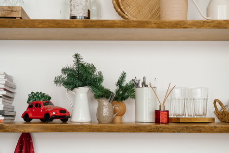 Christmas decor on wooden shelves in the interior of the house: Christmas tree branches in vases, a red toy car, books and a diffuserの写真素材