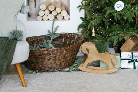 Stylish Christmas decor: a wicker basket with fir branches, gifts and a wooden toy horse under the...