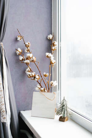 Cotton branches in a vase at the window. Christmas decor in the house. Cozy New Year and winterの写真素材