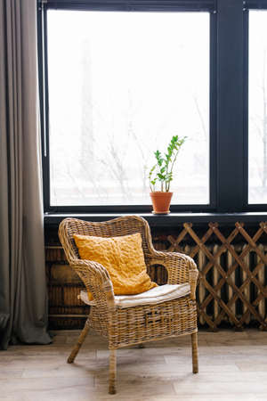 A wicker chair with a yellow mustard cushion next to the window. Cozy atmosphere of the house