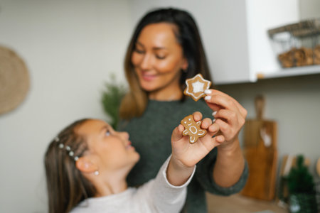 Smiling mom and her daughter are holding Christmas cookies in their kitchenの写真素材