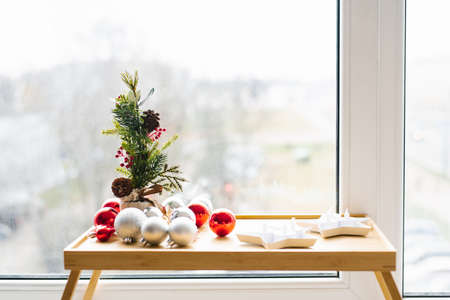 Christmas decor: silver and red Christmas decorations, pine branches on a wooden tray for morning breakfast by the windowの写真素材