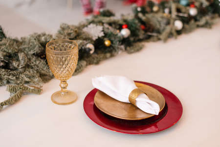 Traditional Christmas table setting. Burgundy and gold plate, linen napkin, fir branches and glass goblet. Festive dinner decorの写真素材