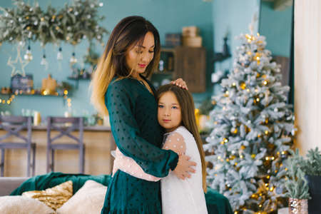 Mom and daughter hug each other in the living room, decorated for Christmas and New Yearの写真素材