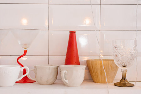 White porcelain or ceramic mugs, wooden crockery, red vase and wine glass on the kitchen shelfの写真素材
