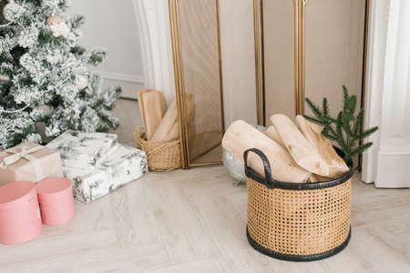 Christmas and New Year decor of the living room: firewood in a basket near the fireplace, gifts under the Christmas treeの写真素材