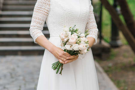 The bride holds a beautiful wedding bouquet of white flowers in her handsの写真素材