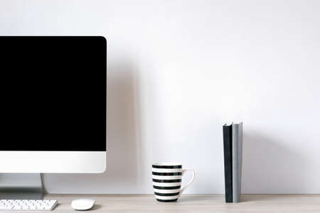 A laptop with a black blank screen, a mug with black and white stripes, notepads is on the desk of...