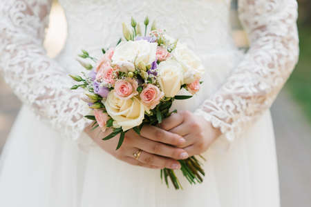 The hands of a young bride are holding a beautiful delicate wedding bouquet. Bride's hand with a wedding ring on her finger. Bride in white dressの写真素材
